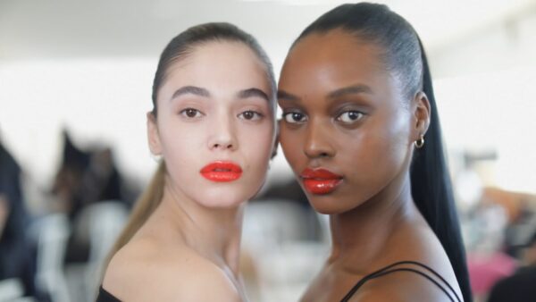 Two models with bright red lips posing for the camera backstage at Miu Miu