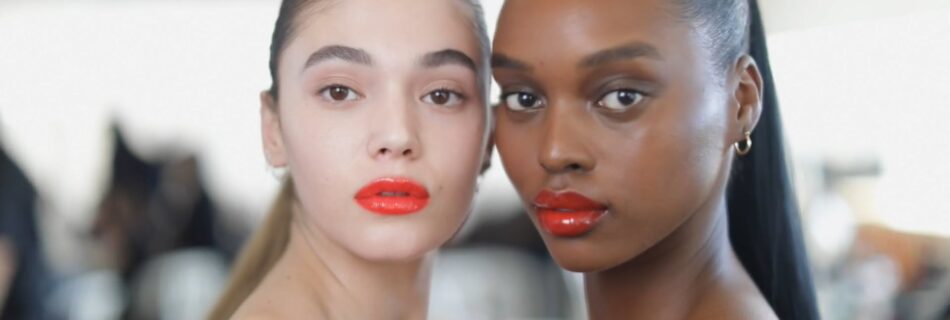 Two models with bright red lips posing for the camera backstage at Miu Miu